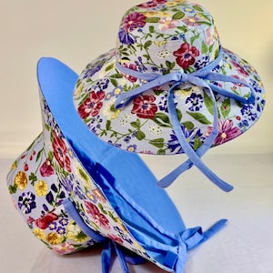 May include: Two blue floral print sun hats with wide brims and matching blue ribbon ties. The hats are made of a lightweight fabric and are perfect for protecting your face and neck from the sun.