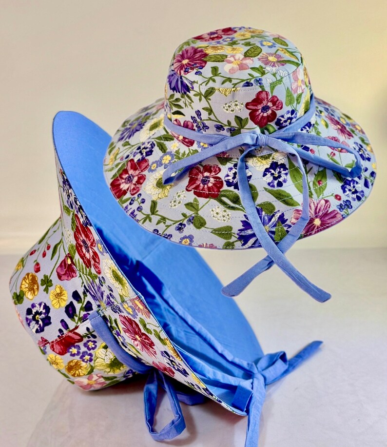 May include: Two blue floral print sun hats with wide brims and matching blue ribbon ties. The hats are made of a lightweight fabric and are perfect for protecting your face and neck from the sun.