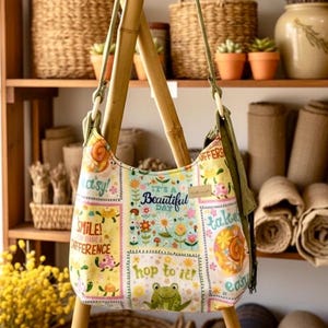 Puede incluir: Bolso de hombro colorido y estampado con un diseño floral y caprichoso. La bolsa presenta el texto "It's a Beautiful Day" y "Hop to it!". La bolsa está suspendida de una estructura de bambú, con cestas y estantes en el fondo.