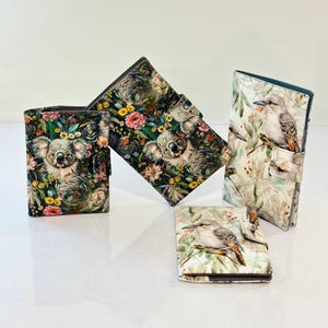 Puede incluir: Cuatro carteras con diseños únicos. Dos carteras presentan un koala rodeado de flores coloridas. Las otras dos carteras muestran un pájaro posado en una rama con hojas verdes. Todas las carteras tienen un borde marrón oscuro.