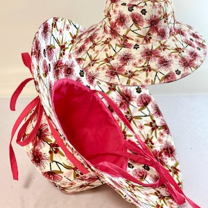 May include: A wide-brimmed sun hat with a pink floral print and a pink lining. The hat has a tie at the back and is folded in half.