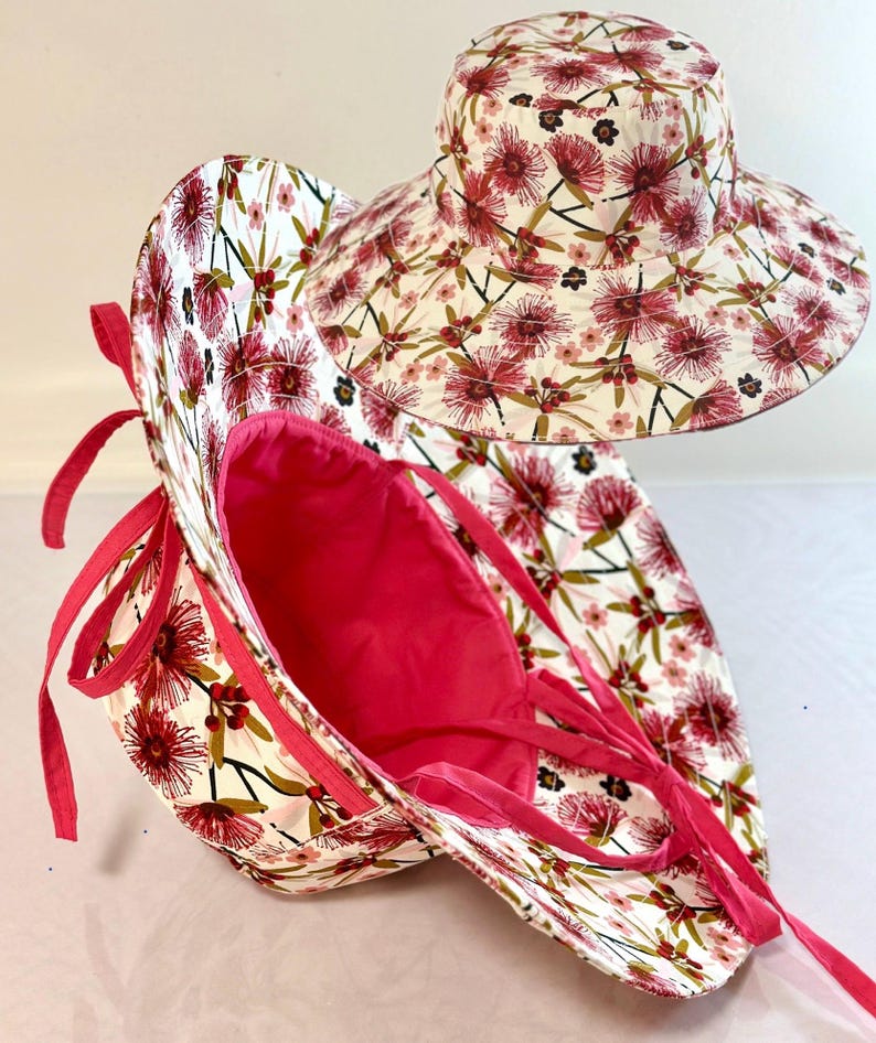 May include: A wide-brimmed sun hat with a pink floral print and a pink lining. The hat has a tie at the back and is folded in half.