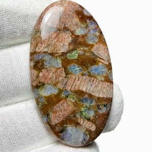 Peut inclure: Une pierre précieuse ovale polie. La pierre présente une mosaïque de couleurs, notamment le marron, le rouge, le bleu et le vert. Le motif a un aspect naturel et organique, avec des variations de texture et de couleur.