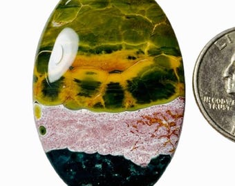 May include: An oval-shaped gemstone with a layered appearance. The top section is green and yellow, followed by a pink band, and a dark blue-green base. A US quarter coin is next to the gemstone for size comparison.