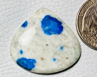 May include: A polished, teardrop-shaped gemstone with a white base and vibrant blue spots. A quarter coin is next to the gemstone for size comparison. The stone has a smooth, glossy surface and is likely a decorative item or jewelry component.