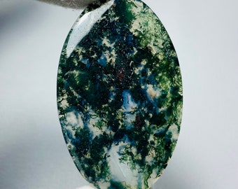 May include: A green, blue, and white moss agate cabochon with a swirling pattern. The cabochon is oval shaped and has a smooth, polished surface.