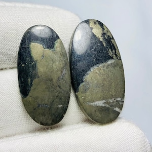 Pode incluir: Dois cabochões ovais de pirita polida com um padrão de mármore preto e dourado.