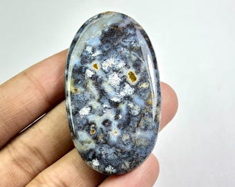 Könnte beinhalten: Ein ovaler Edelstein mit polierter Oberfläche. Der Stein zeigt eine Mischung aus Blau, Weiß, Schwarz und Gold. Das Muster ähnelt einer Landschaft mit wolkenartigen Formationen.