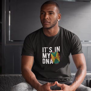 May include: A person wearing a black t-shirt with the text "It's in my DNA" and a graphic of the flag of Dominica.