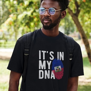 May include: A black t-shirt with the text "IT'S IN MY DNA" in white. A fingerprint with the Haitian flag colors is in the middle of the text.