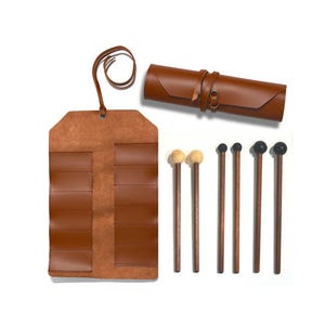 Op de afbeelding: Een verzameling bruinleren percussiehamers en een bijpassende leren hamerkoker. De hamers hebben houten stelen en verschillende koptypes, waaronder vilt en zwart rubber. De koker is opgerold en vastgezet met een leren riem.