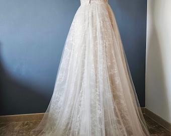 May include: A white strapless wedding dress with a lace bodice and a tulle skirt. The dress has a fitted bodice and a flowing skirt.