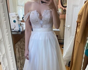 Op de afbeelding: Een witte, off-shoulder bruidsjurk met een kantbovenstuk en een tule rok.