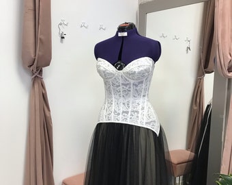 May include: A white lace corset with a black tulle skirt. The corset has a sweetheart neckline and a boned bodice. The skirt is full and flowing.
