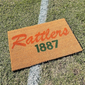 May include: A brown coir doormat with the text "Rattlers 1887" in orange and green lettering.