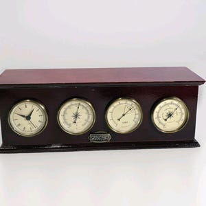 Könnte beinhalten: Eine rechteckige Wetterstation aus dunklem Holz mit vier runden, messinggerahmten Anzeigen. Das Gerät umfasst eine analoge Uhr, ein Thermometer, ein Hygrometer und ein Barometer mit einem kleinen Metallschild Thomas & Thomas London.