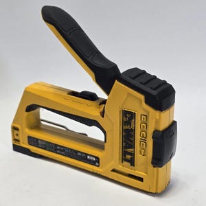 Puede incluir: Una grapadora DEWALT amarilla y negra. La herramienta tiene un mango negro y una parte superior negra. El logotipo de DEWALT está impreso en negro en el lateral. Diseñado para uso intensivo.