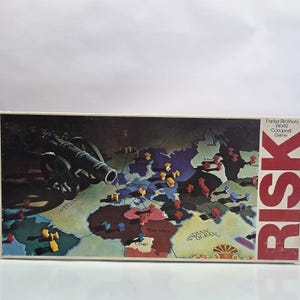 May include: Vintage Parker Brothers Risk board game box. The box features a world map with territories and game pieces. A cannon is depicted on the left side. The word "RISK" is in large red letters on the right side.