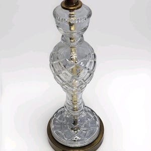 Puede incluir: Lámpara de mesa de cristal transparente con un patrón de corte de diamante en la base y el cuerpo. La lámpara tiene una base y detalles metálicos de color latón. La lámpara es una lámpara decorativa.