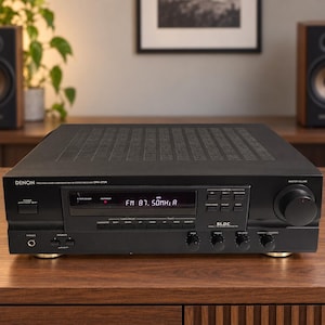 May include: A black Denon DRA-275R stereo receiver featuring a digital display showing FM 87.50MHz, a large master volume knob on the right, multiple function buttons, and control dials for bass, treble, balance, and variable loudness on the front panel.