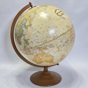 May include: A vintage globe with a cream-coloured sphere displaying geographical details. The globe is mounted on a brown metal stand with a matching meridian and base. The globe features detailed cartography and is a classic educational tool.