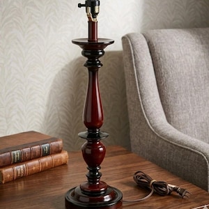 Puede incluir: Lámpara de mesa roja oscura y negra con un diseño clásico. La lámpara tiene un portalámparas y una base redonda. La lámpara está sobre una mesa de madera. Mide unos 40 cm de altura.