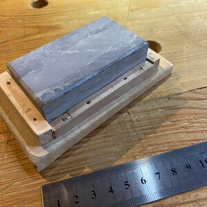 Peut inclure: Une pierre &agrave; aiguiser grise est mont&eacute;e sur une base en bois de forme rectangulaire. La base est de couleur brun clair et est en bois. La pierre est mont&eacute;e dans la base &agrave; l'aide de vis.