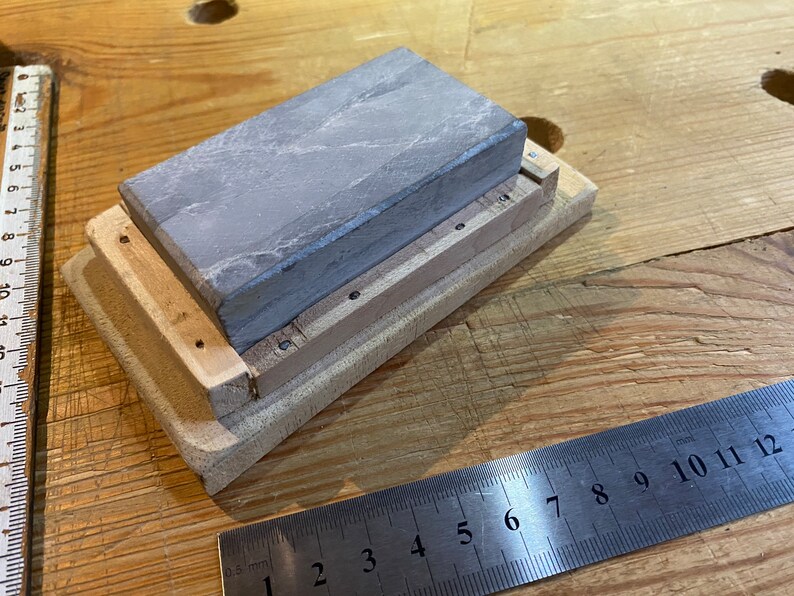 Peut inclure: Une pierre &agrave; aiguiser grise est mont&eacute;e sur une base en bois de forme rectangulaire. La base est de couleur brun clair et est en bois. La pierre est mont&eacute;e dans la base &agrave; l'aide de vis.