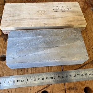 Puede incluir: Una piedra de afilar rectangular de piedra de Creta gris, que mide aproximadamente 71 cm de largo, con una caja de madera con la etiqueta "Cretan Stone 2024 gr weight made 2011".