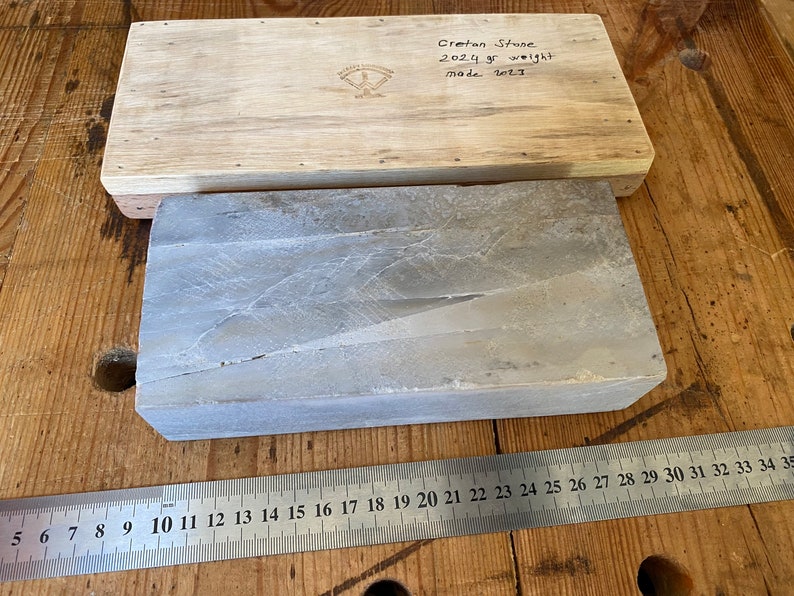 Puede incluir: Una piedra de afilar rectangular de piedra de Creta gris, que mide aproximadamente 71 cm de largo, con una caja de madera con la etiqueta "Cretan Stone 2024 gr weight made 2011".