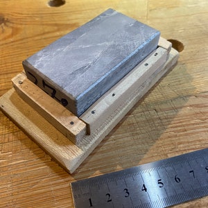 Peut inclure: Une pierre &agrave; aiguiser grise est mont&eacute;e sur une base en bois avec un petit cadre en bois autour. La pierre est &eacute;tiquet&eacute;e "0.70".