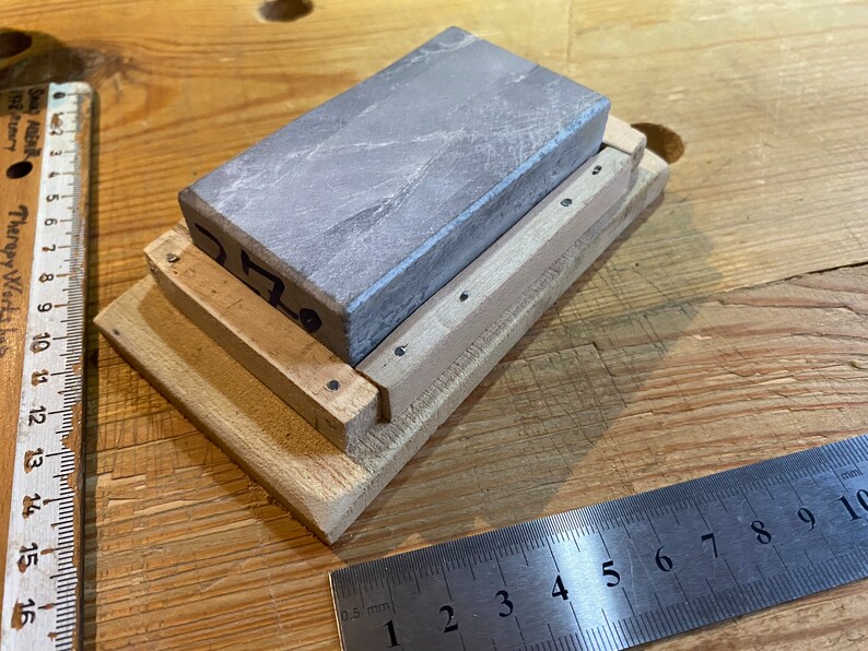 Peut inclure: Une pierre &agrave; aiguiser grise est mont&eacute;e sur une base en bois avec un petit cadre en bois autour. La pierre est &eacute;tiquet&eacute;e "0.70".