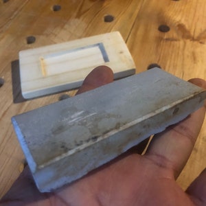 May include: A grey rectangular sharpening stone with a slightly rough texture.
