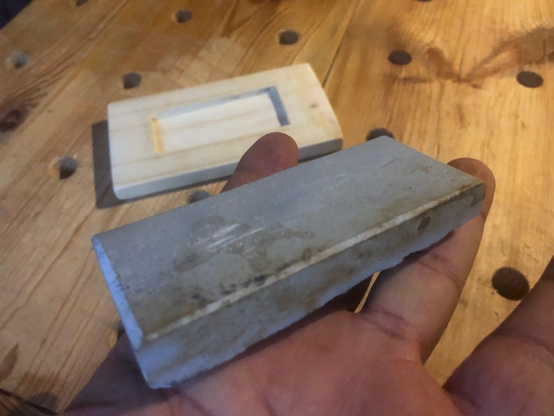 May include: A grey rectangular sharpening stone with a slightly rough texture.