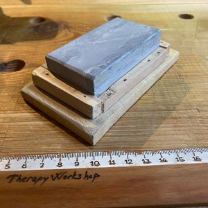 Peut inclure: Une pierre &agrave; aiguiser grise avec une base en bois. La base est compos&eacute;e de trois couches de bois, chacune avec un motif de grain diff&eacute;rent. La pierre mesure environ 15 cm de long et 5 cm de large.
