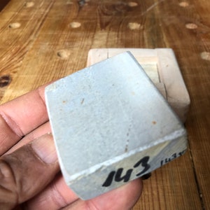 Pu&ograve; includere: Una pietra per affilare rettangolare grigia con il numero "143" scritto su di essa con un pennarello nero.