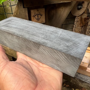 May include: A rectangular block of grey stone with a textured, scratched surface. The stone has a matte finish and visible linear markings across its top and side faces, showing a consistent grey color throughout the solid, dense material.