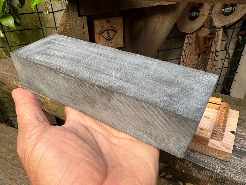 May include: A rectangular block of grey stone with a textured, scratched surface. The stone has a matte finish and visible linear markings across its top and side faces, showing a consistent grey color throughout the solid, dense material.