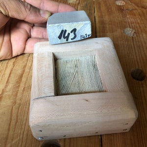Pu&ograve; includere: Una scatola di legno con un'apertura rettangolare, progettata per contenere una pietra per affilare grigia. La pietra &egrave; etichettata "143".