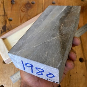 Puede incluir: Una piedra de afilar rectangular gris con una inscripci&oacute;n azul que dice "1980".