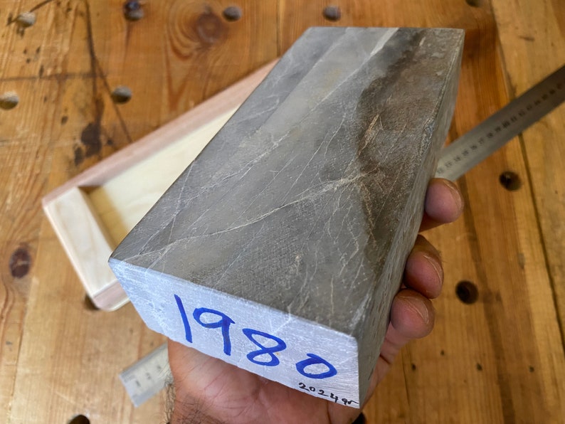 Puede incluir: Una piedra de afilar rectangular gris con una inscripci&oacute;n azul que dice "1980".