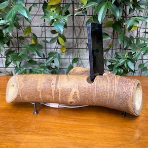 May include: A wooden phone stand shaped like a tree branch with a black smartphone in the stand.