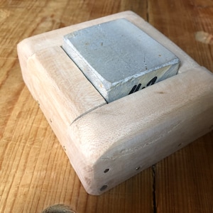 Pu&ograve; includere: Una pietra per affilare rettangolare di colore grigio chiaro &egrave; tenuta in una cornice di legno. La cornice &egrave; in legno chiaro e ha una finitura liscia. La pietra &egrave; etichettata con "#2".