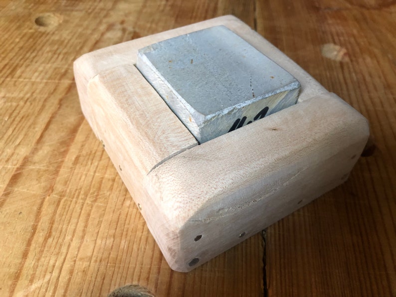 Pu&ograve; includere: Una pietra per affilare rettangolare di colore grigio chiaro &egrave; tenuta in una cornice di legno. La cornice &egrave; in legno chiaro e ha una finitura liscia. La pietra &egrave; etichettata con "#2".