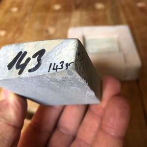 Pu&ograve; includere: Una pietra per affilare rettangolare grigia con i numeri "143" e "143g" scritti su di essa con un pennarello nero.