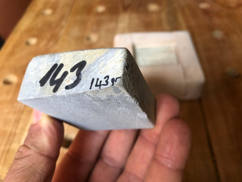 Pu&ograve; includere: Una pietra per affilare rettangolare grigia con i numeri "143" e "143g" scritti su di essa con un pennarello nero.