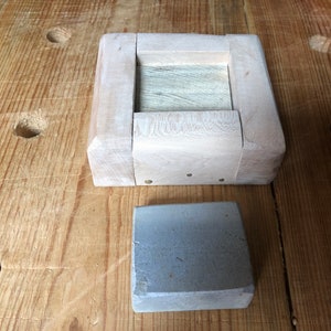 Pu&ograve; includere: Una scatola di legno con un sasso grigio all'interno. La scatola &egrave; fatta di legno chiaro e ha un design semplice. Il sasso &egrave; rettangolare e ha una texture ruvida.