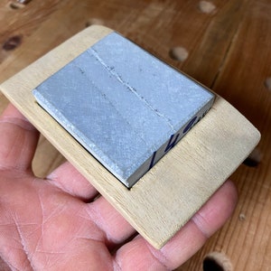 May include: A light gray rectangular sharpening stone is set into a wooden frame. The frame is made of light wood and has a slightly rounded edge.