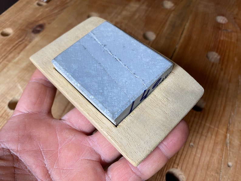 May include: A light gray rectangular sharpening stone is set into a wooden frame. The frame is made of light wood and has a slightly rounded edge.
