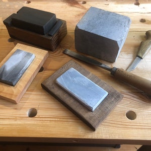 May include: Four sharpening stones, two in wooden frames, one in a wooden box, and one loose. A wooden handled chisel with a blue tip and the text "HITACHI" on the handle. A wooden handled knife with a brown handle.